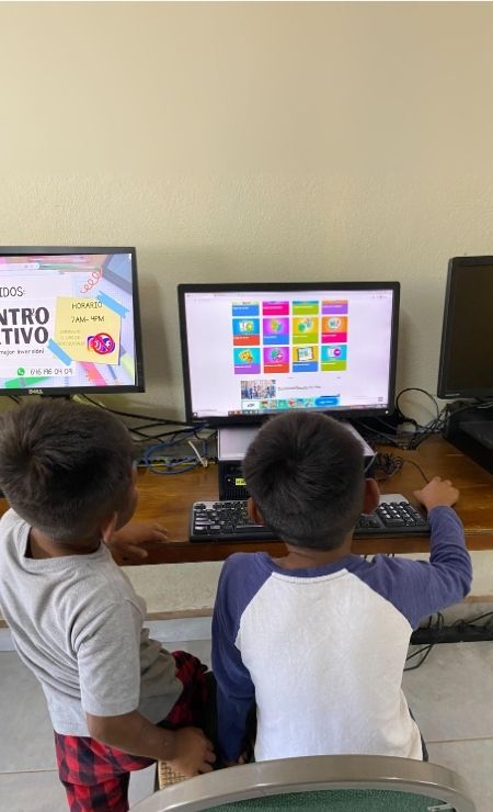 Two children engaged with a computer, exploring educational software on the screen, highlighting the impact of computer donations on education in Mexico.