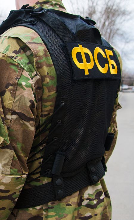 Military personnel in camouflage uniform wearing a tactical vest with "ФСБ" insignia, indicating a security or law enforcement context.