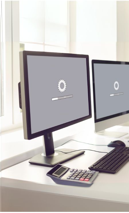 Computer monitor displaying loading gear icon, symbolizing a slow computer issue, with keyboard and calculator on desk, relevant to tips on optimizing PC performance.