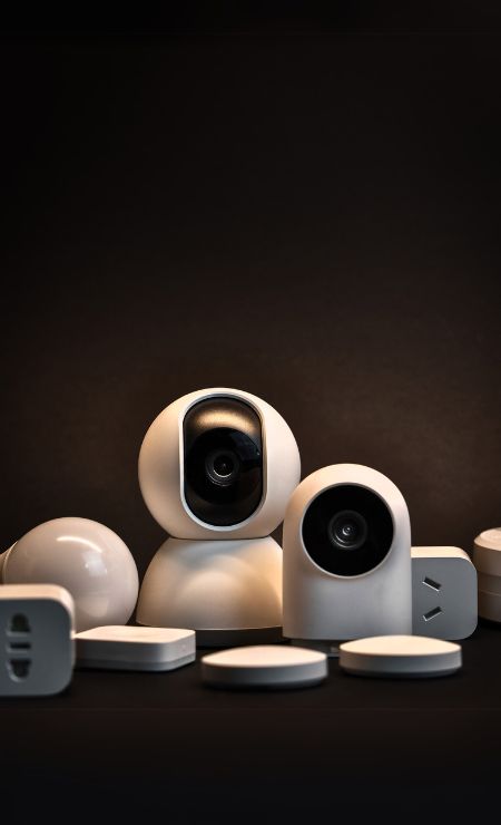 IoT devices including security cameras and smart plugs on a dark background, representing cybersecurity risks and solutions for businesses.